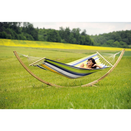 Person relaxing in a colourful hammock with a wooden arc in a grassy field.